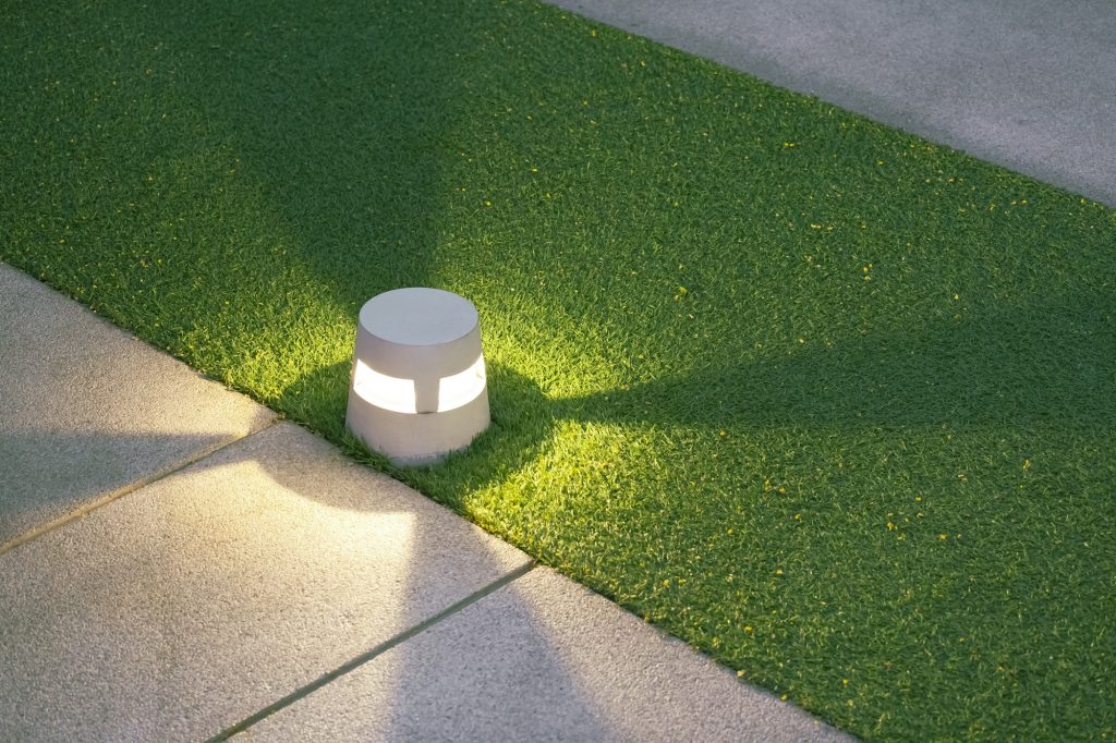 Illuminated LED ground lantern on artificial turf and gravel stone walkway in the evening park Illuminated LED ground lantern on artificial turf and gravel stone walkway in the evening park