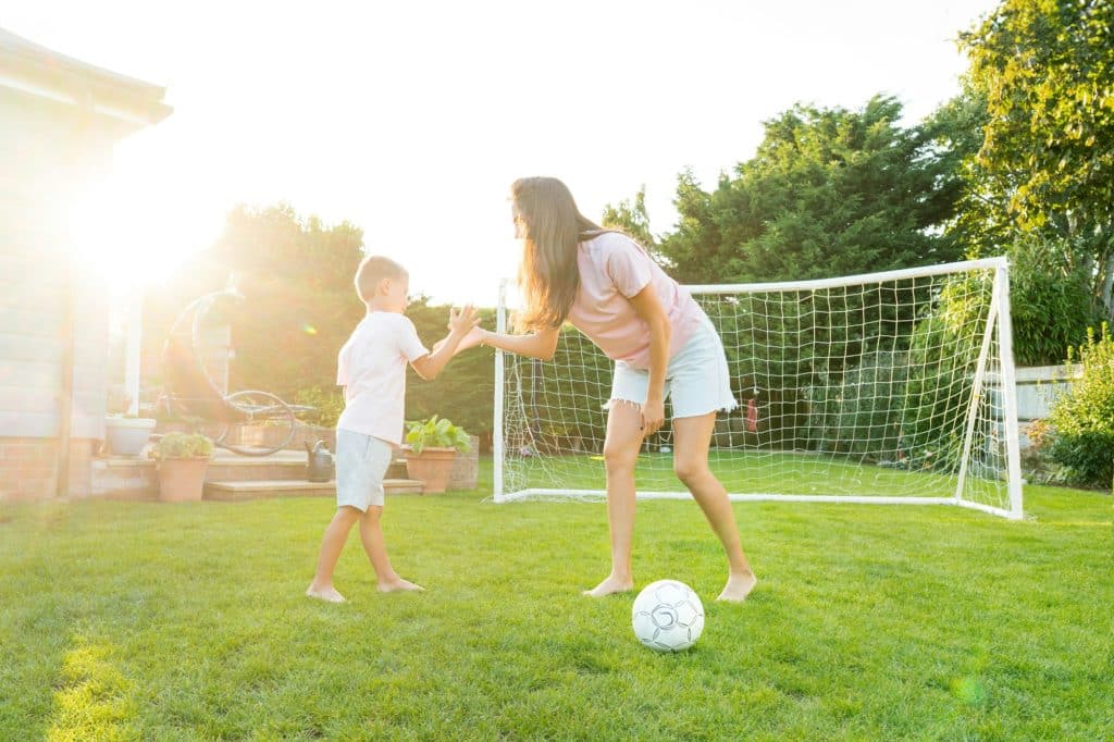 Young mother and son giving five during soccer game in the garden. Happy family playing football Young mother and son giving five during soccer game in the garden. Happy family playing football